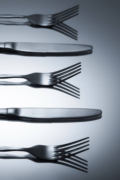 close-up view of shiny forks and knives reflected on grey    