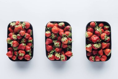 Beyaz yüzeyinde plastik kaplar olgun çilek ile satır üstten görünüm