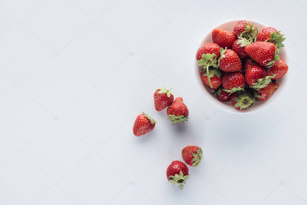 top view of bowl of fresh whole strawberries on white surface