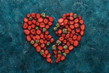 top view of halved heart sign made of ripe strawberries on blue concrete surface clipart