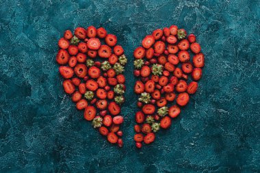 top view of halved heart sign made of strawberries on blue concrete surface clipart