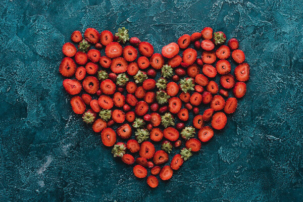 top view of heart sign made of ripe strawberries on blue concrete surface