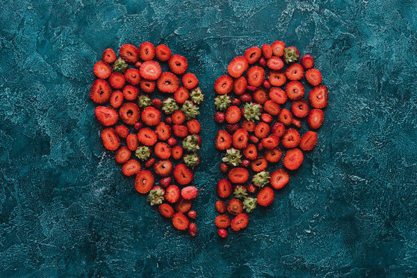 top view of halved heart sign made of strawberries on blue concrete surface