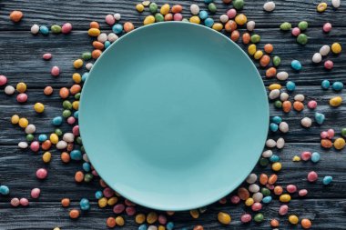 top view of empty plate surrounded by colorful candies on wooden table  clipart