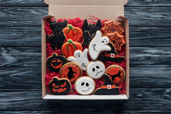 elevated view of cardboard box with homemade halloween cookies on wooden table 