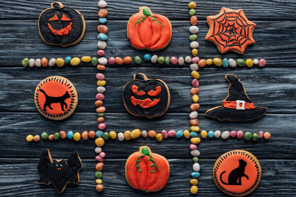 вид сверху на композицию из разноцветных конфет и устроенную кулинарию Хэллоуина на деревянном столе
 