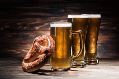 glasses of beer and tasty pretzel on wooden surface, oktoberfest concept clipart