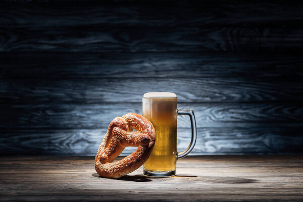 glass of fresh beer and tasty pretzel on wooden table, oktoberfest concept