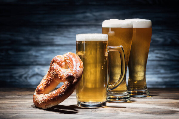 three glasses of beer with foam and tasty pretzel on tabletop, oktoberfest concept