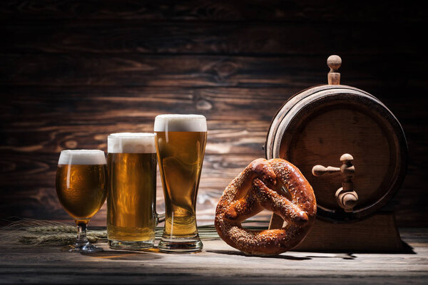 glasses of beer, tasty pretzel and beer barrel on wooden table, oktoberfest concept