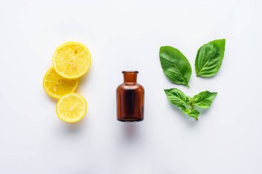 şişe doğal bitkisel uçucu yağ, limon parçaları ve yeşil yaprakları üzerinde beyaz izole üstten görünüm