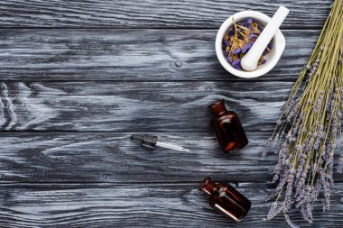 top view of bottles of natural herbal essential oils, dropper and dried flowers on wooden table clipart