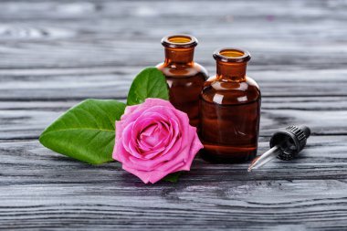 bottles of natural herbal essential oils, pipette and pink rose on wooden surface clipart