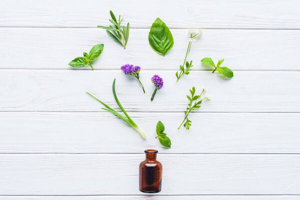 top view of bottle of natural herbal essential oil and scattered green leaves on white wooden tabletop