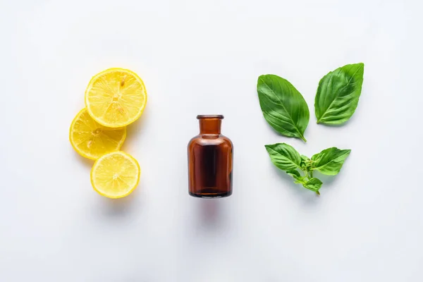şişe doğal bitkisel uçucu yağ, limon parçaları ve yeşil yaprakları üzerinde beyaz izole üstten görünüm
