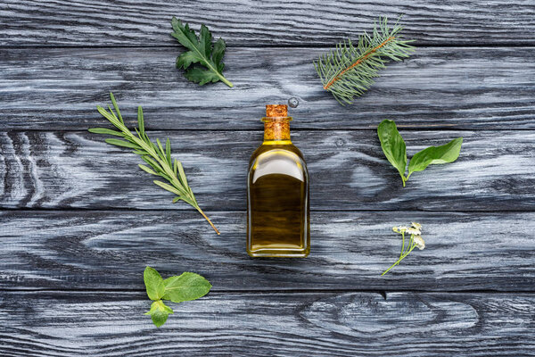 elevated view of bottle of natural herbal essential oil and green leaves on wooden surface