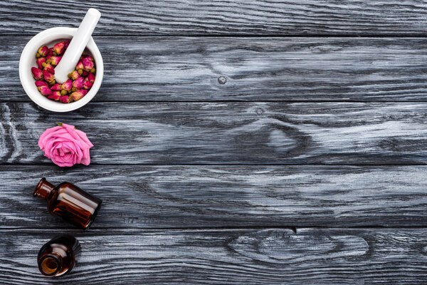 elevated view of bottles of natural herbal essential oils and roses on grey surface 