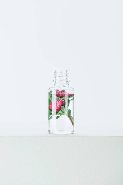 bottle of natural herbal essential oil with flowers on white surface
