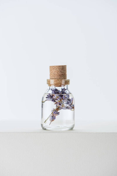 bottle of natural herbal essential oil with violet flowers on white surface