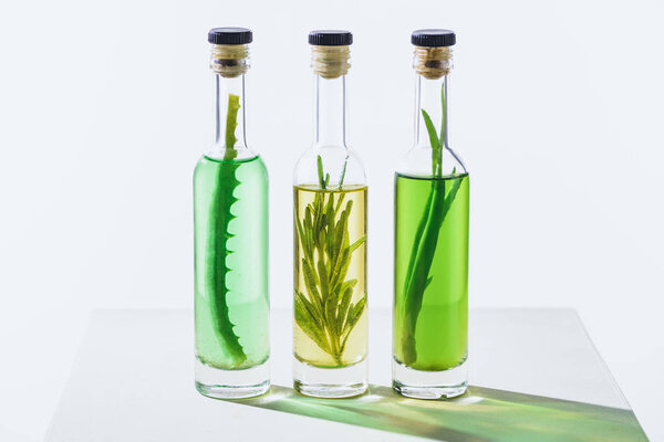 transparent bottles of essential green and yellow oils with plants on white surface