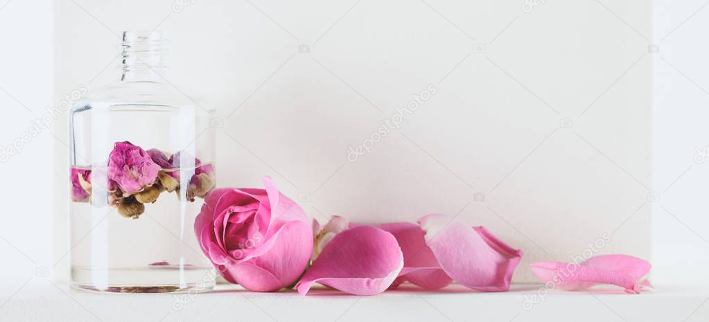 bottle of natural herbal essential oil with pink roses on white surface
