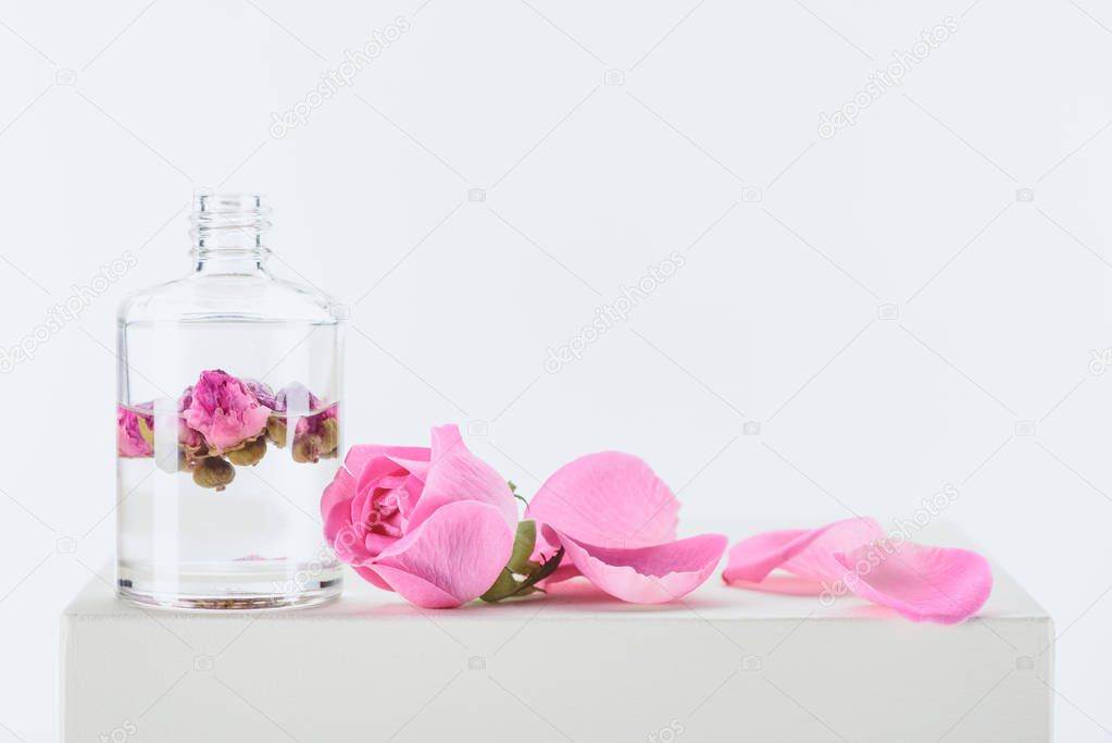 bottle of aromatic essential oil with pink roses on white surface