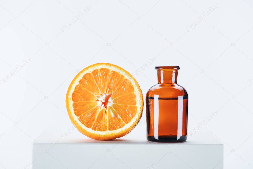bottle of natural herbal essential oil and cut orange on white cube