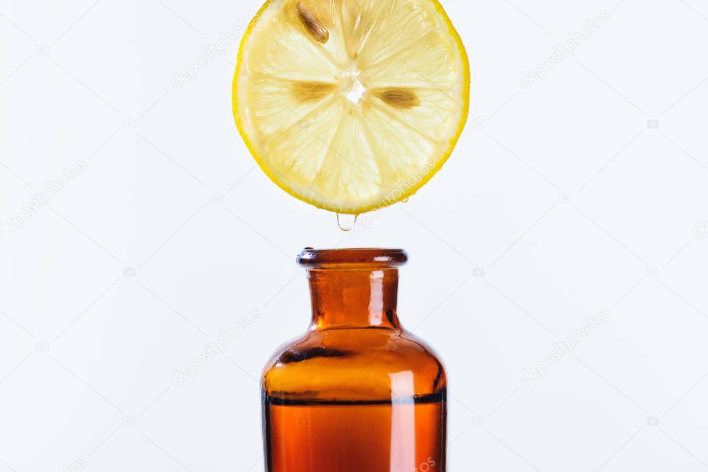 aromatic juice of lemon piece dripping into bottle of natural herbal essential oil isolated on white