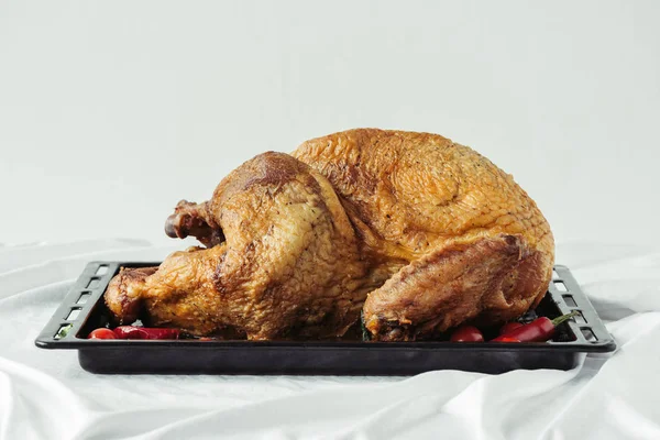 close up view of cooked festive turkey on baking pan on surface with tablecloth on grey background, thanksgiving holiday dinner concept