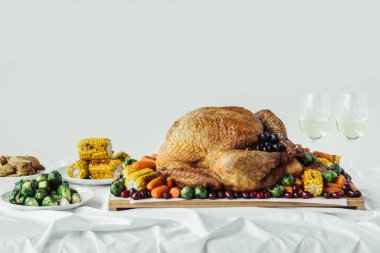 close up view of holiday dinner table set with roasted turkey, vegetables and glasses of wine on grey background, thanksgiving holiday concept