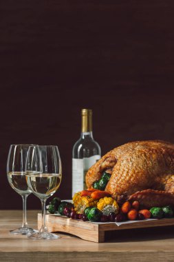 close up view of traditional roasted turkey, vegetables and glasses of wine for thanksgiving dinner
