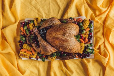 top view of roasted festive turkey and vegetables on tabletop with yellow tablecloth, thanksgiving holiday concept clipart
