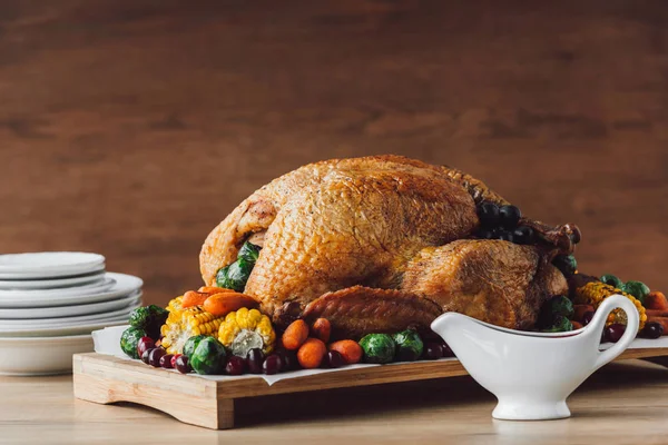 close up view of roasted turkey with vegetables, sauce and cutlery on wooden surface, thanksgiving holiday concept