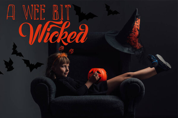 adorable kid in halloween costume resting in armchair in dark room with "a wee bit wicked" lettering