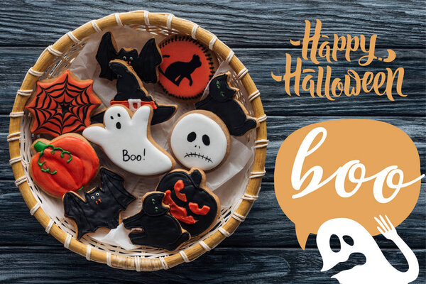 Top view of wicker basket with homemade spooky halloween cookies on wooden table with "happy halloween" and ghost with "Boo" lettering
