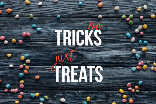 elevated view of arranged colorful delicious candies on wooden background  with "no tricks just treats" lettering