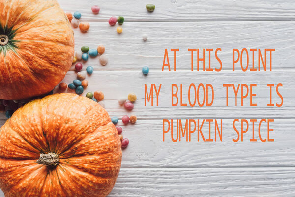 верхний вид тыквы и красочные конфеты на деревянном фоне с надписью "на данный момент моя группа крови тыквенные пряности"
