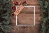 pohled shora bílý rámeček, vánoční dárek a lesklé cetky na dřevěný povrch s jedle větvičky a šišky