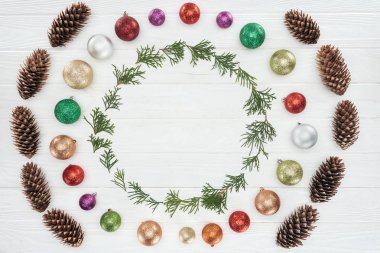 evergreen coniferous twigs, pine cones and shiny colorful baubles on white wooden background