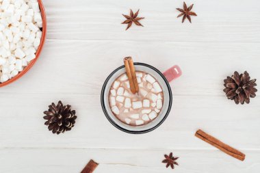 top view of cup with hot chocolate and marshmallows, cinnamon sticks, star anise and pine cones on wooden table  clipart