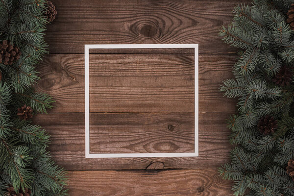 верхний вид на белый каркас и вечнозеленые ветки с сосновыми шишками на деревянном фоне
