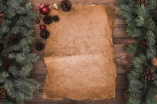 blank parchment with fir twigs, shiny baubles and pine cones on wooden background 