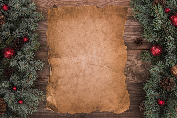 close-up view of blank parchment with fir twigs, shiny baubles and pine cones on wooden background 