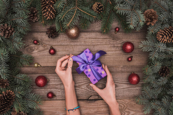 cropped shot of person opening christmas present on wooden surface with festive decorations