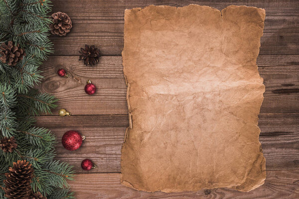 top view of blank parchment, coniferous branches with pine cones and baubles, christmas background