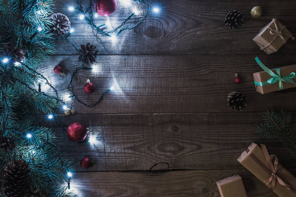 christmas presents, shiny baubles and fir twigs with illuminated garland on wooden background 