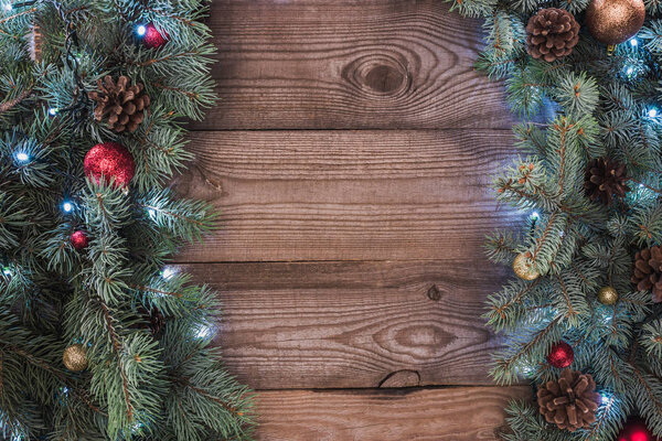 top view of coniferous twigs with shiny baubles, pine cones and illuminated garland, christmas background