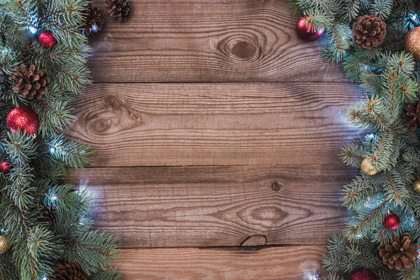 beautiful christmas tree branches with baubles, pine cones and illuminated garland on wooden background 