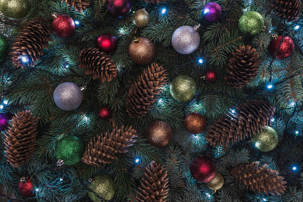 close-up view of beautiful christmas tree with pine cones, colorful balls and illuminated garland 