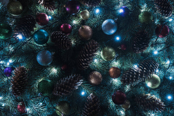 close-up view of beautiful christmas tree with pine cones, colorful baubles and illuminated garland 
